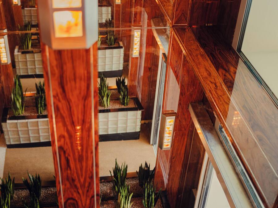 A modern hotel lobby with a central atrium, wooden columns, and floor-to-ceiling windows.