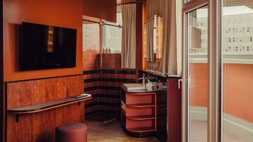 A modern bathroom with a wooden vanity, a mirror, a sink, and a television mounted on the wall.