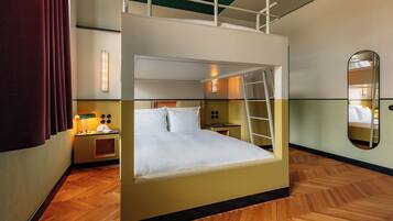 A bunk bed room with a ladder, a nightstand, a lamp, and a mirror.