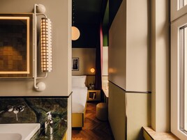 Casa de banho moderna com bancada de mármore, lavatório branco, espelho com toalha e mesa de cabeceira com candeeiro.