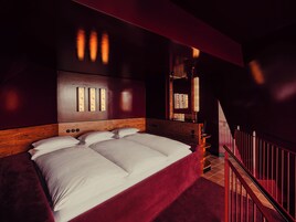 Una camera da letto con un letto grande, una testiera in legno, una parete di accentazione rossa e una scala con ringhiere rosse.