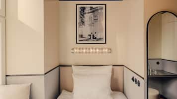 Cama bem arrumada com lençóis brancos, uma fotografia a preto e branco emoldurada acima e uma mesa de cabeceira com um candeeiro.