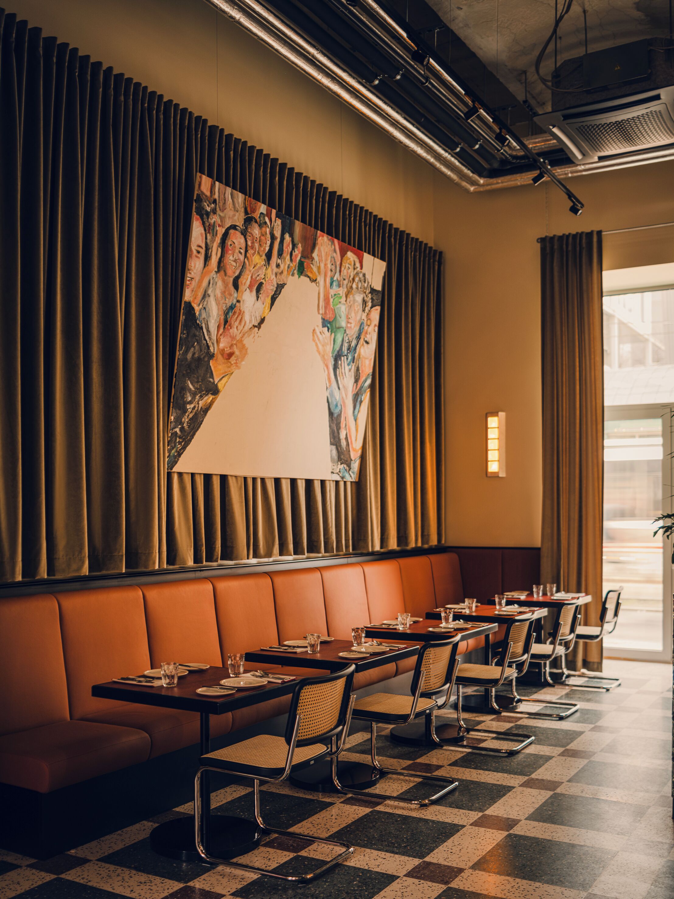 A restaurant with a checkered floor, leather booth seating, and a large abstract painting on the wall.
