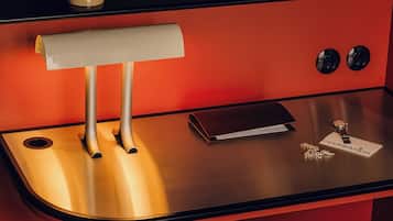 Een kleine hotelkamer met een stapelbed, een bureau met lamp, een klein tafeltje, een stoel en een nachtkastje met horloge en sleutels.