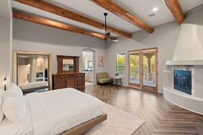 A spacious bedroom with a large bed, wooden beams, a fireplace, and a view of the outdoors.