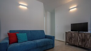A modern living room with a blue sofa, a flat-screen TV, and built-in lighting. - Super cosy apartment near the sea for 6/8 people (Follonica)