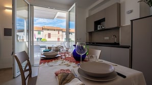A dining area with a table set for two, a window with a view of buildings, and a kitchen with modern appliances. - Super cosy apartment near the sea for 6/8 people (Follonica)
