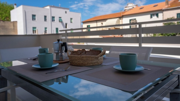 A balcony with a table set for two, a coffee maker, and a basket of bread. - Super cosy apartment near the sea for 6/8 people (Follonica)