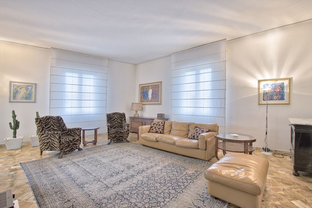 A spacious living room with a large patterned rug, a beige sofa, a zebra-patterned armchair, and a small round table.
