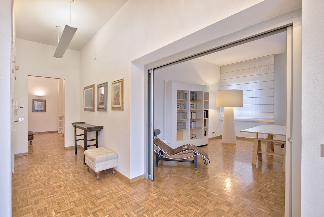 A spacious room with a wooden parquet floor, a white bench, a reading chair, and a bookshelf.