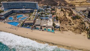 An aerial view of a resort with multiple swimming pools, beachfront, and a large hotel building. - 6BR Luxe Villa w/ Infinity Pool & Ocean Views (Cabo San Lucas)