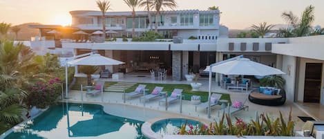 Una casa moderna con piscina, mobiliario exterior y palmeras.
