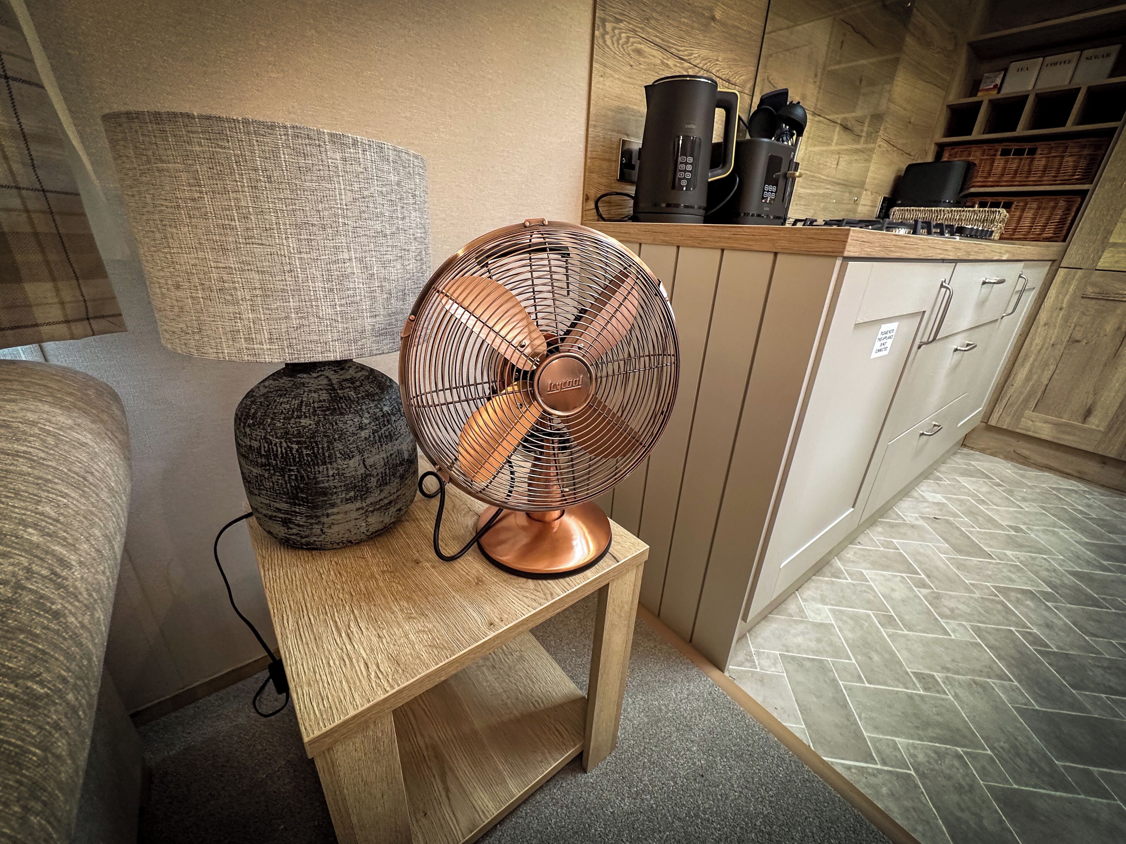 Une cuisine avec une table en bois, un ventilateur, une lampe au design original et une machine à café.