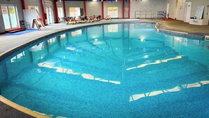 Una piscina interior con agua cristalina, borde de azulejos y un puesto de socorrista.