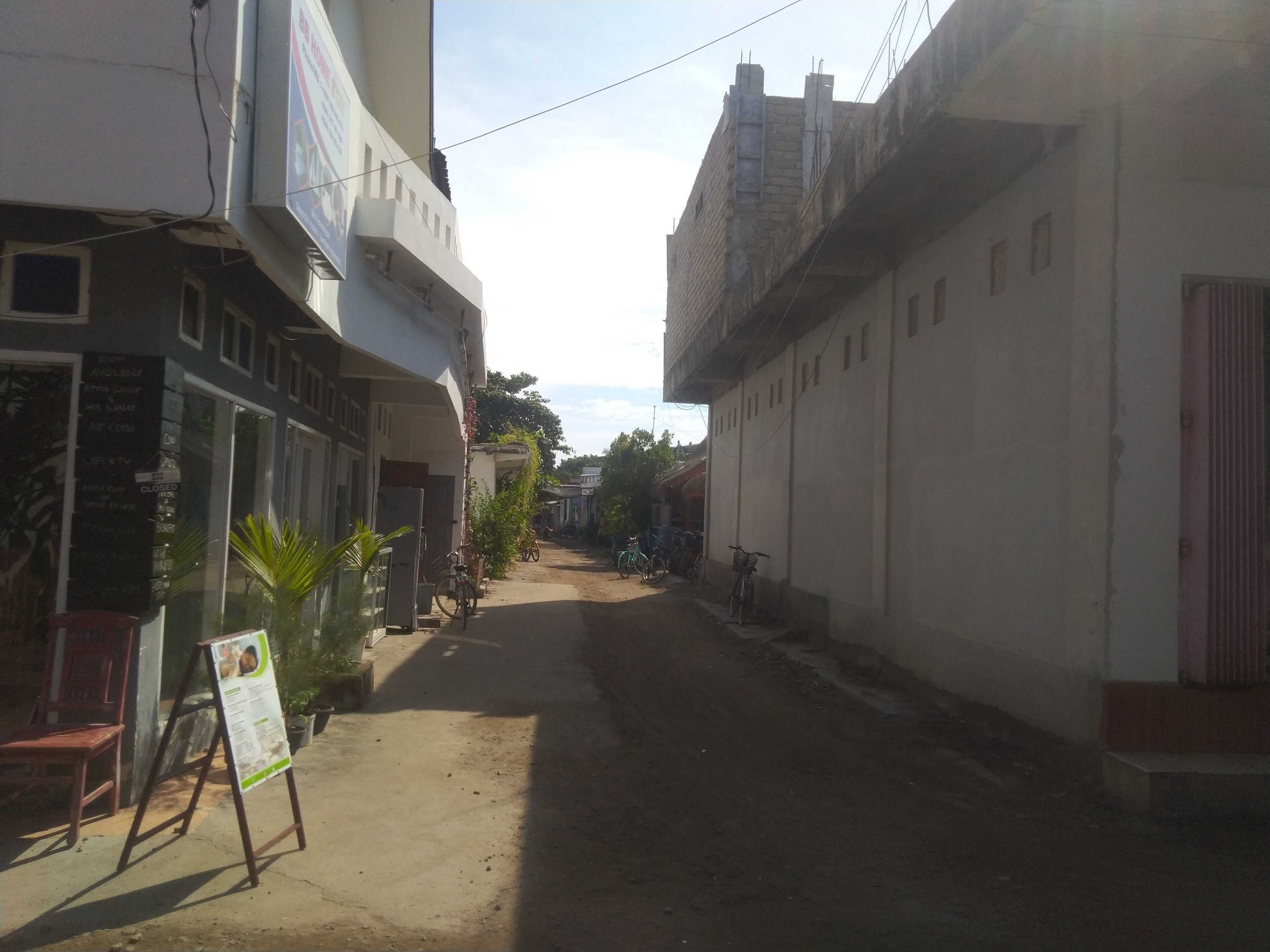 A narrow street with buildings on either side, a signboard, and a bicycle parked on the right.