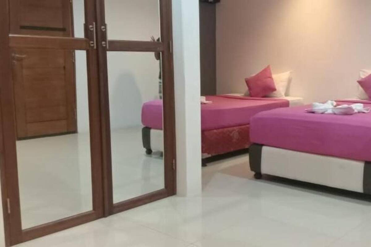 A hotel room with two beds, each with a pink bedspread and pillows, a wooden door, and a white tiled floor.