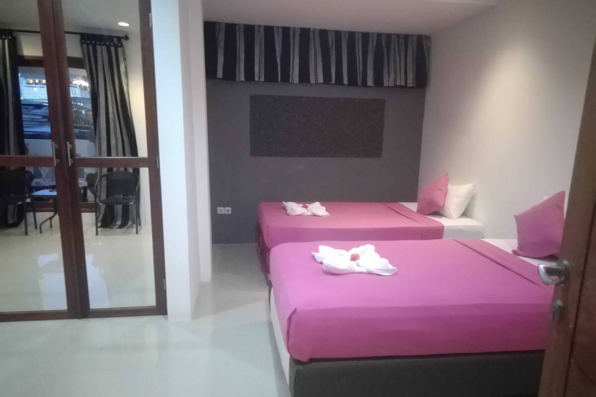 A hotel room with two beds, a large window with curtains, a flat-screen TV, and a seating area with chairs and a table.