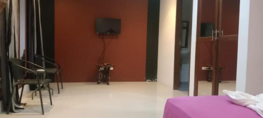 A room with a bed, a TV mounted on the wall, a small table with a speaker, and a chair.