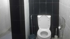 A bathroom with a white toilet, a black trash bin, and a toilet brush.
