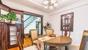 A dining area with a round table, chairs, a chandelier, and a staircase in the background.