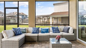 A covered outdoor seating area with a sectional sofa and a glass coffee table.