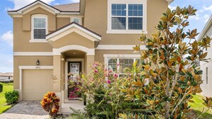 A two-story house with a beige exterior, a garage, and a well-maintained front yard with various plants and flowers.
