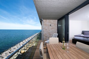 Ein Balkon mit Meerblick, ein Holztisch mit Flasche und Glas sowie eine Couch.