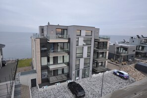 Ein modernes, mehrgeschossiges Wohngebäude mit Balkonen, einem Parkplatz und Blick auf das Meer.