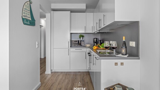 A modern kitchen with white cabinetry, a wooden floor, and a countertop with kitchen appliances and a bottle of wine. - Küstenglück - Shower room, covered balcony, garden furniture, TV, parking space (Damp)