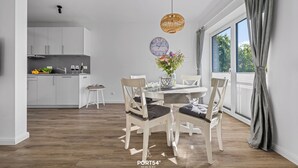 A modern kitchen with white cabinets and a dining area with a wooden table and chairs. - Küstenglück - Shower room, covered balcony, garden furniture, TV, parking space (Damp)