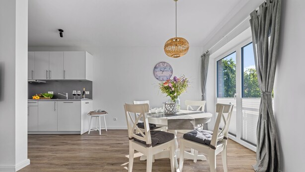Une cuisine moderne avec des meubles blancs et un coin repas comprenant une table et des chaises en bois.