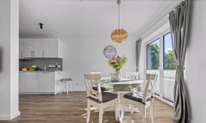 A modern kitchen with white cabinets and a dining area with a wooden table and chairs. - Küstenglück - Shower room, covered balcony, garden furniture, TV, parking space (Damp)