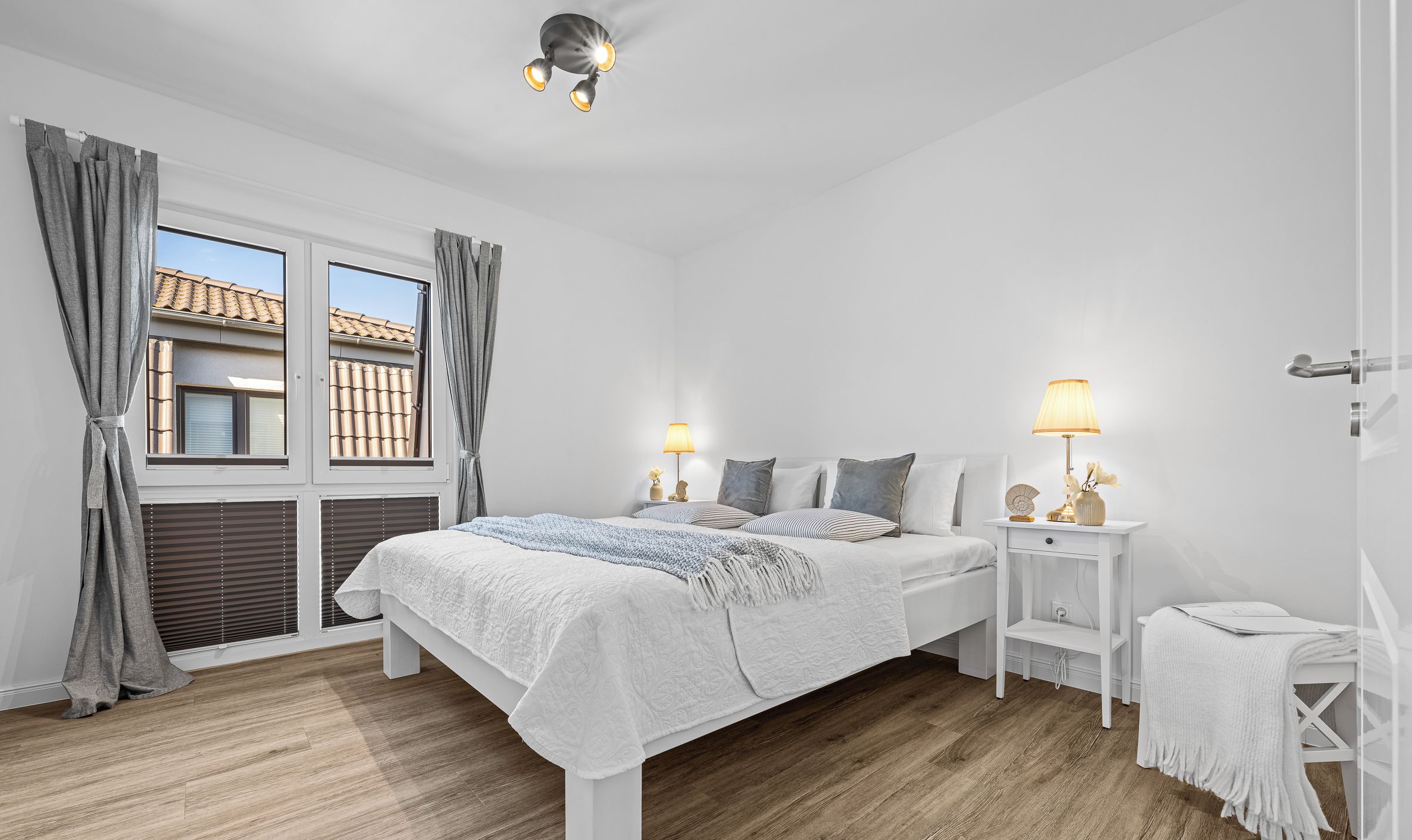A bedroom with a bed, bedside tables, a nightstand, a window with curtains, and a ceiling light fixture.