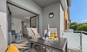 Un balcón con una mesa de madera, sillas y un cuenco de fruta.