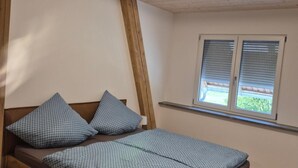 Een slaapkamer met een houten bed, een raam met zonwering en een schuine kap.