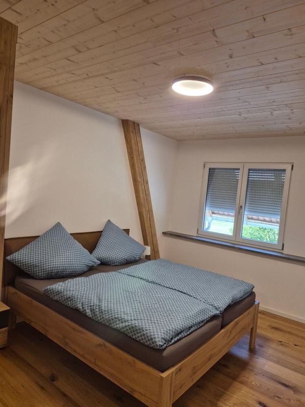 Un dormitorio con cama de madera, una ventana con persianas y techo inclinado.