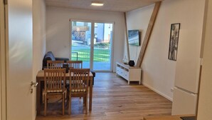 Een moderne keuken met houten vloeren, een eethoek met een tafel en stoelen, en een uitzicht door een glazen deur op een buitenruimte.