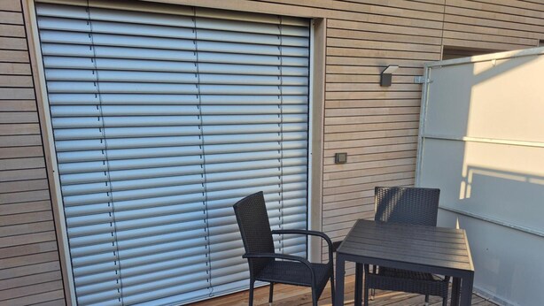 Een terras met een tafel en stoelen, een schuifdeur en een wandlamp.