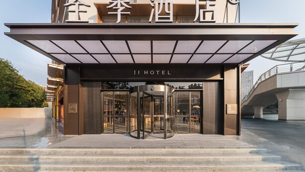 L’entrée d’un hôtel, avec une porte tournante, une enseigne avec des caractères chinois et une façade moderne en verre.
