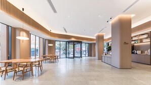 Un hall d’entrée spacieux avec un espace salon aménagé en cercle, de grandes fenêtres et une cuisine moderne visible au fond.