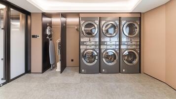 A laundry room with four stacked front-loading washing machines, a drying machine, and a wall-mounted fan.