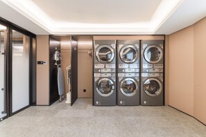 A laundry room with four stacked front-loading washing machines, a drying machine, and a wall-mounted fan. - Ji Hotel Guangzhou Shayuan Metro Station (Guangzhou)