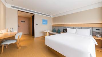 A hotel room with a large bed, a desk with a chair, a small round table, and a nightstand with a lamp.