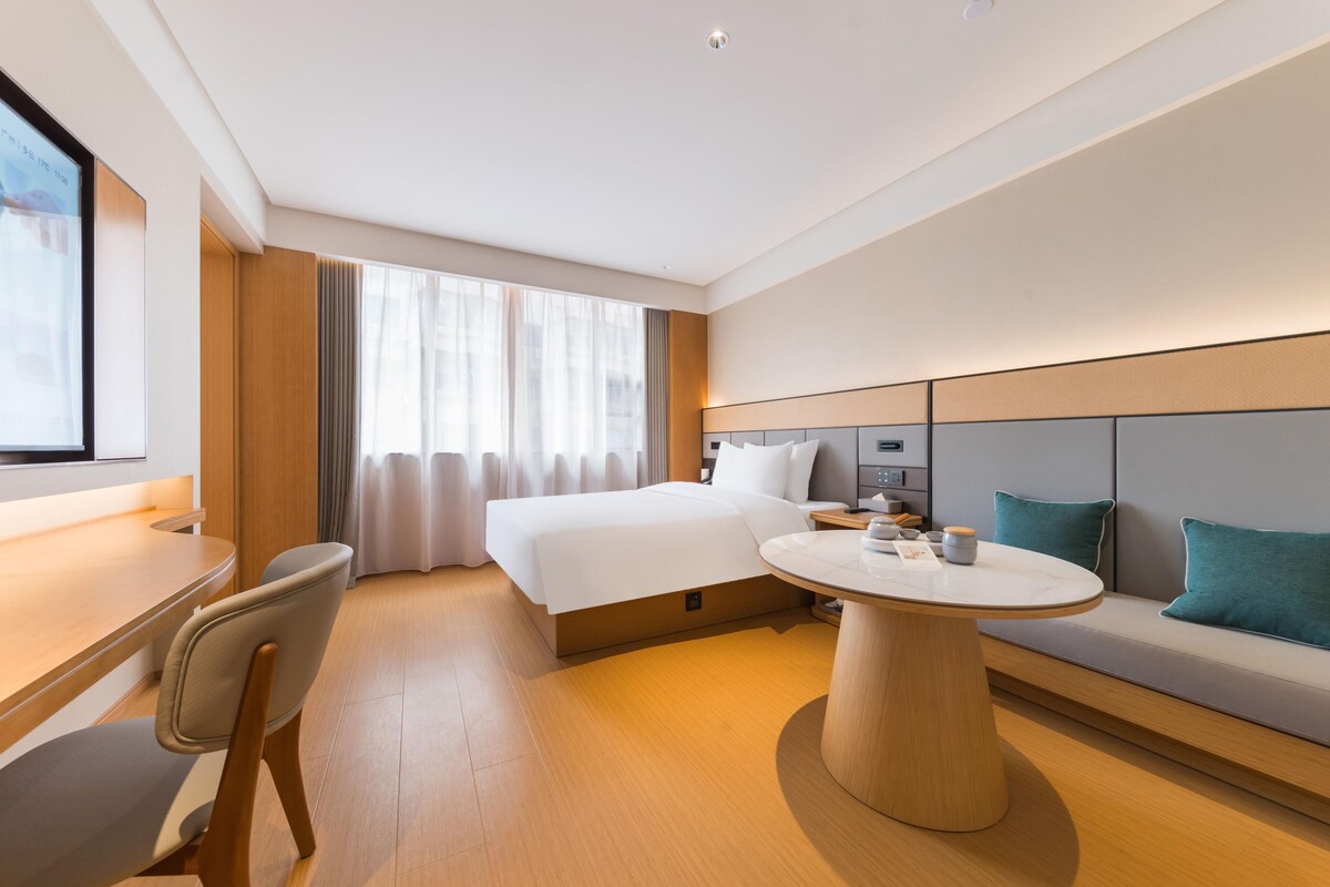 A modern hotel room with a bed, a dining table, a sofa, and a TV.