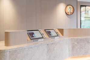 A reception desk with two digital kiosks, a wooden panel wall, and a circular sign with Chinese characters. - Ji Hotel Guangzhou Shayuan Metro Station (Guangzhou)