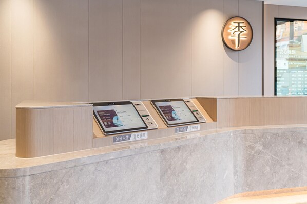 A reception desk with two digital kiosks, a wooden panel wall, and a circular sign with Chinese characters. - Ji Hotel Guangzhou Shayuan Metro Station (Guangzhou)