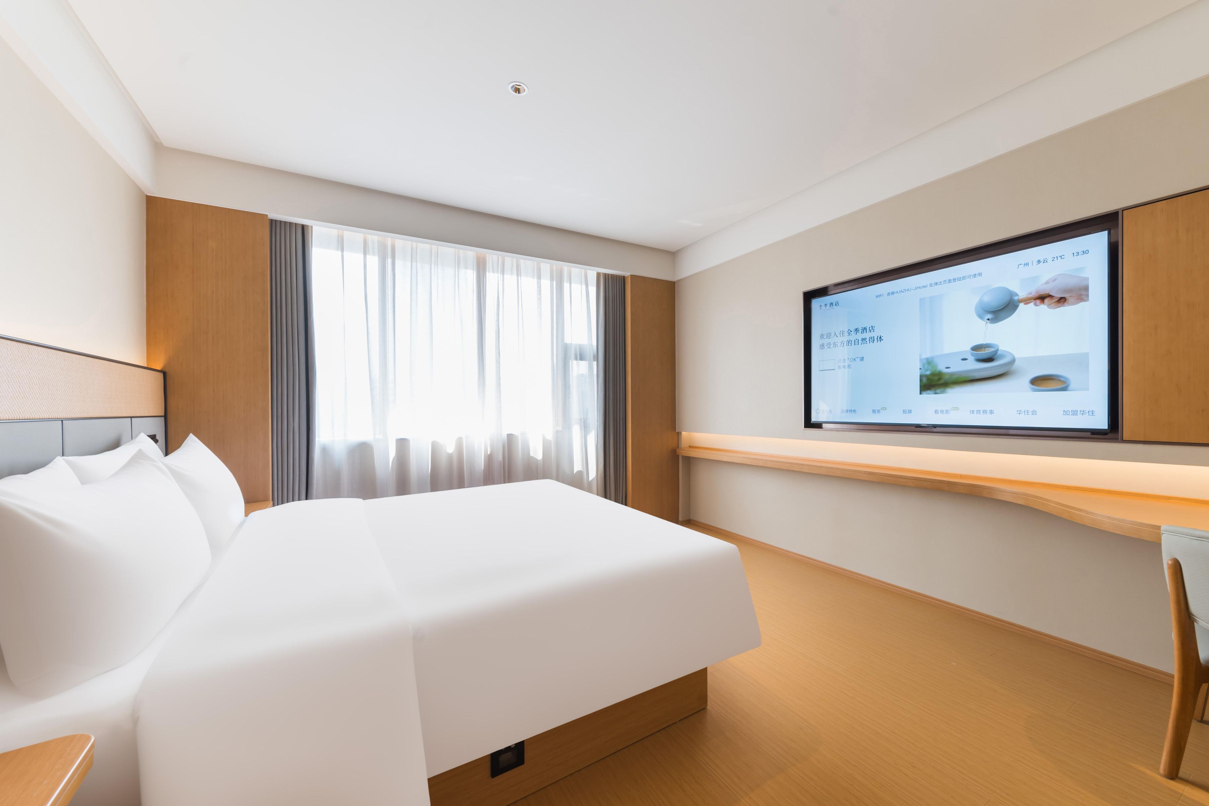 Una habitación de hotel moderna con una cama grande, un televisor de pantalla plana montado en la pared y un escritorio de madera.