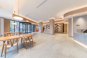 A spacious, modern interior with a long wooden table and chairs, a reception desk, and a well-lit area with large windows. - Ji Hotel Guangzhou Shayuan Metro Station (Guangzhou)