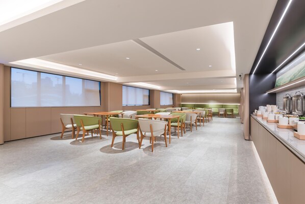 A modern dining area with multiple tables and chairs, large windows, and a kitchen counter with various items. - Ji Hotel Guangzhou Shayuan Metro Station (Guangzhou)