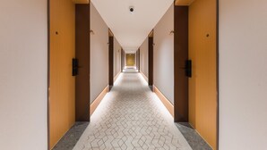 Un long couloir étroit, typique des hôtels, avec des portes en bois de chaque côté et un sol à motifs.